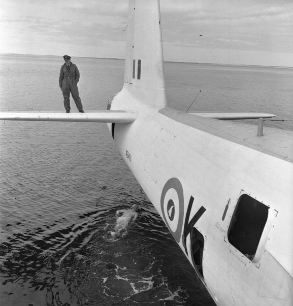 PR2183-R2-6-59 Salvage of Maritime Operational Conversion Unit Sunderland, NZ4111, after it was holed and sank in Te Whanga Lagoon, Chatham Islands. Wing Commander Henry Lionel Homer, Director of Aircraft Engineering, doing an exterior underwater inspection of the Sunderland, while Squadron Leader Robert Emery Weston (?) watches from the starboard horizontal stabiliser. NB. this negative deteriorating resulting in poorer image quality.