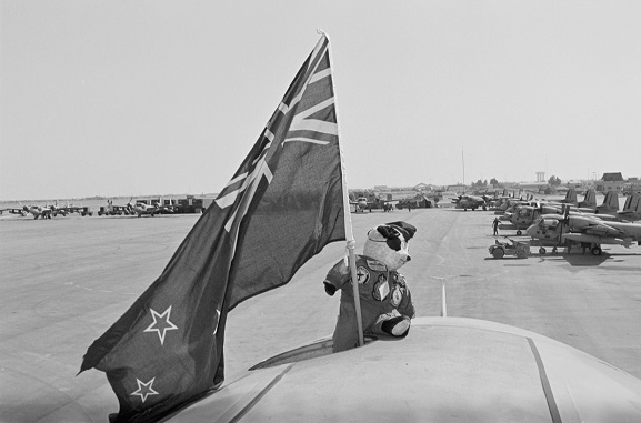 PD13-9-91 No. 75 Squadron RNZAF mascot, Henry Fanshaw, 'on deployment' with No. 40 Squadron, proudly waving a New Zealand flag atop a 40 Squadron Hercules. Riyadh, Saudi Arabia.
In the background are US Army Grumman Mohawk aircraft. Operation Fresco, Feb-Mar 1991. Image ref. PD13-9-91, RNZAF Official.