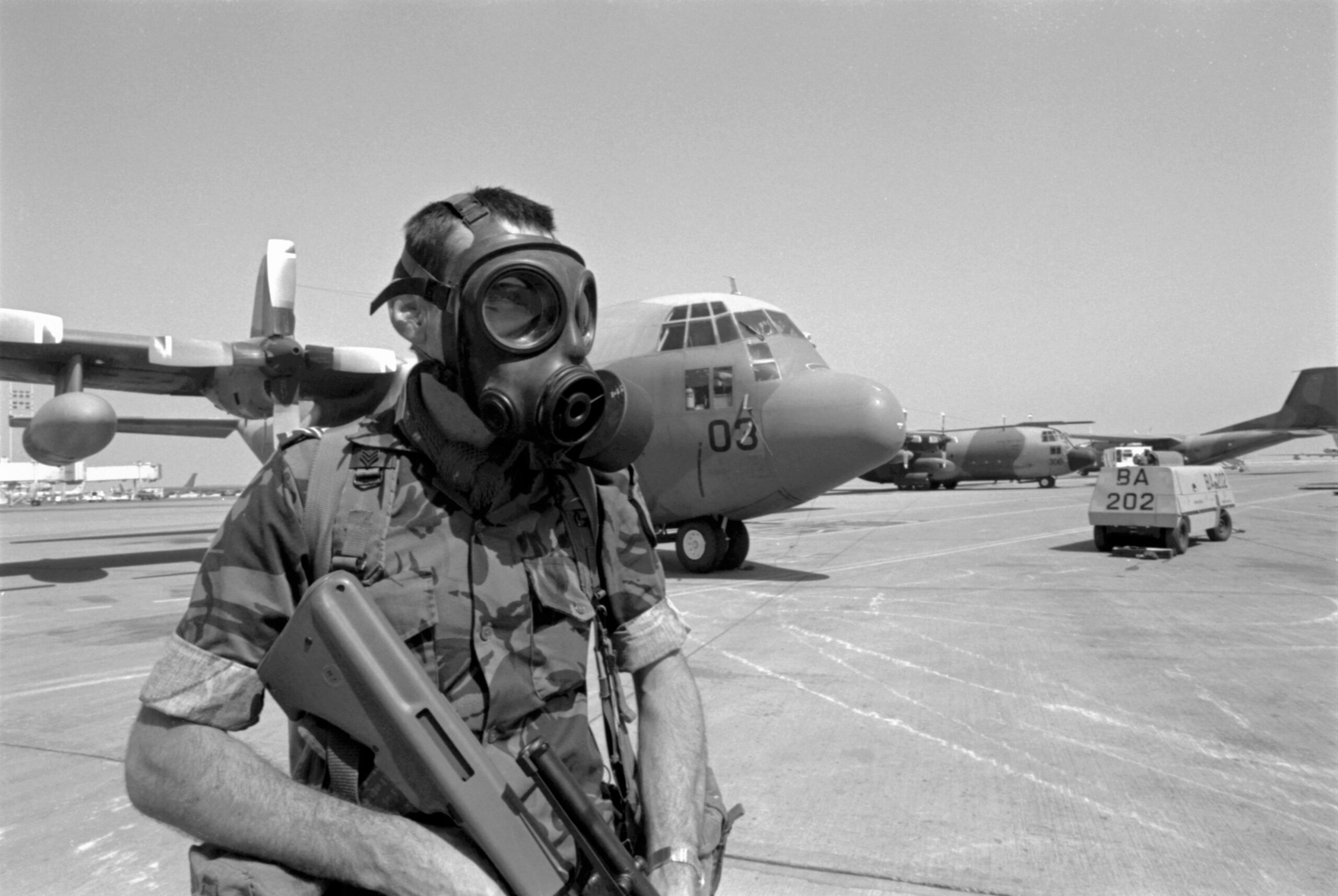 PD14-2-91 Sergeant Phil Lane, wearing a gas mask, on security duty on the tarmac in front of No. 40 Squadron Hercules NZ7003. Riyadh, Saudi Arabia, Feb-Mar 1991. Image ref PD14-2-91, RNZAF Official.